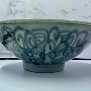 May include: A ceramic bowl with a light blue and white color scheme. The bowl features a decorative blue swirl pattern around the exterior. The bowl has a rounded shape with a slightly flared rim and a small foot.