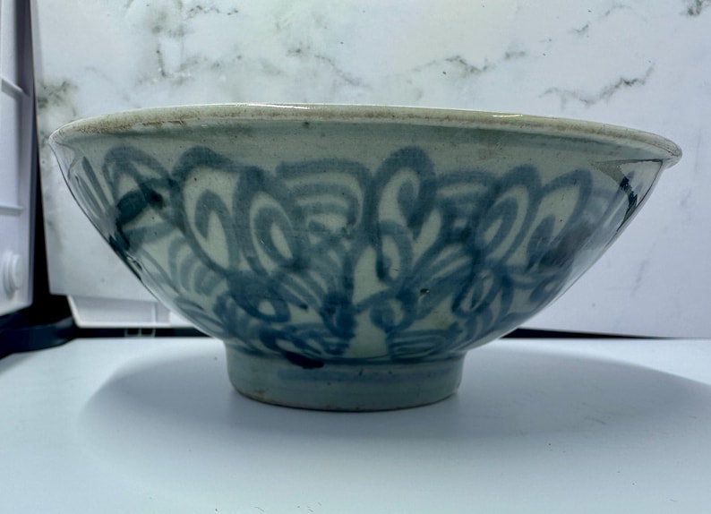 May include: A ceramic bowl with a light blue and white color scheme. The bowl features a decorative blue swirl pattern around the exterior. The bowl has a rounded shape with a slightly flared rim and a small foot.