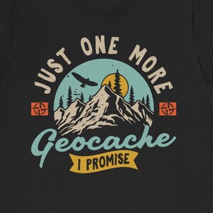 May include: Black t-shirt with a vintage-style graphic of a mountain range, a flying bird, and a compass. The text reads "Just One More Geocache I Promise".