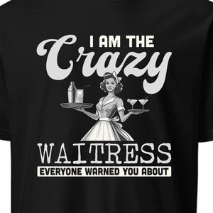 May include: Black t-shirt with a graphic of a waitress holding a tray with drinks. The text reads "I AM THE CRAZY WAITRESS EVERYONE WARNED YOU ABOUT" in white lettering. The design is a vintage style.
