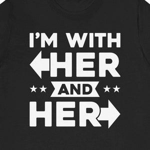 Op de afbeelding: Zwart T-shirt met witte tekst die "I'm with her and her" zegt met pijlen die naar links en rechts wijzen.