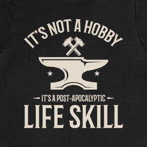 May include: Black t-shirt with a white graphic design of an anvil and crossed hammers. The text reads "It's not a hobby - It's a post-apocalyptic life skill."