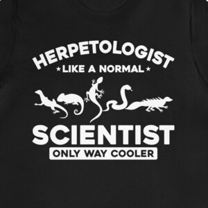 May include: Black t-shirt with white text that reads "Herpetologist *like a normal* Scientist Only Way Cooler". The text is surrounded by images of lizards, snakes, and a salamander.