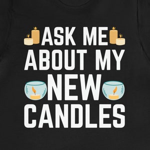 Könnte beinhalten: Schwarzes T-Shirt mit weißem Text, der "Ask me about my new candles" lautet. Der Text ist von Bildern von Kerzen umgeben.