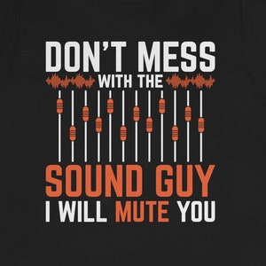 Pode incluir: Camiseta preta com texto branco que diz "Don't mess with the sound guy I will mute you". O texto é cercado por um gráfico de uma mesa de mistura com deslizadores laranja.