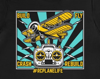 Op de afbeelding: Zwart T-shirt met een afbeelding van een geel vliegtuig dat over een blauw-wit gestreepte achtergrond vliegt. De tekst "BUILD FLY CRASH REBUILD #RCPLANELIFE" staat op het T-shirt gedrukt.