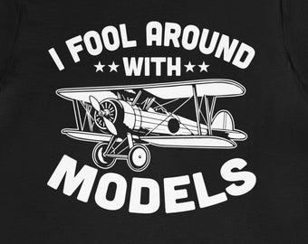 Op de afbeelding: Zwart T-shirt met witte tekst die "I fool around with *** MODELS" luidt en een wit silhouet van een klein vliegtuig.