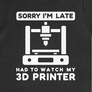 May include: A dark heather grey t-shirt with a white graphic of a 3D printer and the text "Sorry I'm late, had to watch my 3D printer".