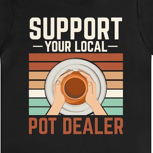 May include: Black t-shirt with a retro design featuring a person making pottery on a wheel. The text reads "Support Your Local Pot Dealer".