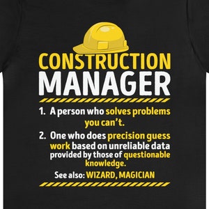 May include: Black t-shirt with a yellow construction worker helmet graphic and the text "CONSTRUCTION MANAGER". The text below the graphic reads: "1. A person who solves problems you can't. 2. One who does precision guess work based on unreliable data provided by those of questionable knowledge. See also: WIZARD, MAGICIAN"