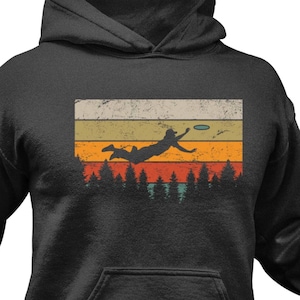 May include: A dark grey hoodie with a vintage-style graphic of a person throwing a frisbee in front of a sunset. The graphic has a retro color scheme with orange, yellow, and blue.