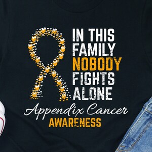 May include: Black t-shirt with a yellow ribbon made of hearts and the text "In this family nobody fights alone. Appendix Cancer Awareness."