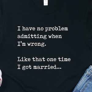 May include: Black t-shirt with white text that reads "I have no problem admitting when I'm wrong. Like that one time I got married..."