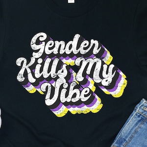 May include: Black t-shirt with a retro-style graphic that says "Gender Kills My Vibe" in yellow, purple, and white lettering. The graphic is on a black background and has a distressed look.