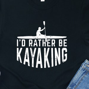 May include: A black t-shirt with a white graphic of a person kayaking and the text "I'd rather be kayaking".