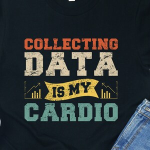 Może przedstawiać: Czarny T-shirt z grafiką w stylu vintage, na której widnieje napis "Collecting Data Is My Cardio". Grafika przedstawia żółty i czerwony wykres słupkowy ze strzałką skierowaną w górę.