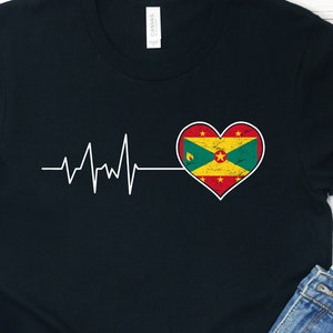 Może przedstawiać: Czarny T-shirt z białym wzorem bicia serca i czerwonym, żółtym i zielonym sercem z flagą Grenady w środku. Serce jest lekko zużyte.