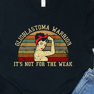 May include: Black t-shirt with a vintage-style graphic of a woman with a red bandana and the text "Glioblastoma Warrior" and "It's not for the weak".