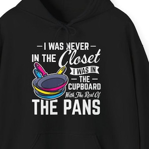 Pode incluir: Moletom preto com estampa frontal. A estampa apresenta uma pilha de panelas coloridas e o texto "-I WAS NEVER- IN THE Closet I WAS IN -THE- CUPBOARD With The Rest Of THE PANS."