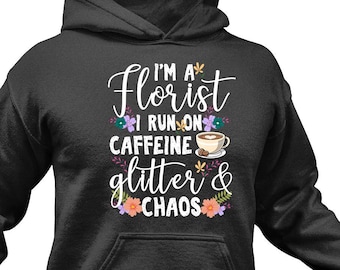 Peut inclure: Un sweat-shirt à capuche noir avec un motif blanc qui dit "I'm a Florist I run on Caffeine Glitter & Chaos" avec une tasse de café et des accents floraux.