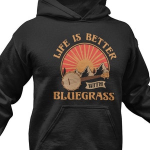 May include: Black hooded sweatshirt with a graphic print of a banjo, mountains, and a sunset. The text reads "Life is better with bluegrass".