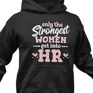 Peut inclure: Sweat-shirt à capuche noir avec le texte "Only the Strongest Women get into... HR" en blanc avec des cœurs roses de chaque côté du texte.