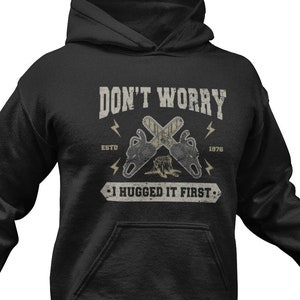 May include: Black hooded sweatshirt with a graphic print of two crossed chainsaws and the text "Don't Worry I Hugged It First".