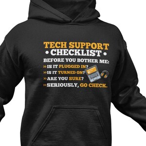 Pode incluir: Camisola de capuz preta com texto branco que diz "TECH SUPPORT • CHECKLIST." O texto continua com uma lista de perguntas: "BEFORE YOU BOTHER ME:  >>> IS IT PLUGGED IN? >>> IS IT TURNED ON? >>> ARE YOU SURE? >>> SERIOUSLY, GO CHECK."