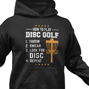 May include: Black hooded sweatshirt with a white graphic print that says "How to play Disc Golf" with a list of steps: "1. Throw, 2. Swear, 3. Look for Disc, 4. Repeat".