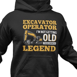 Peut inclure: Sweat-shirt à capuche noir avec un graphique d'excavatrice jaune et le texte "Excavator Operator I'm not getting old I'm becoming a legend".