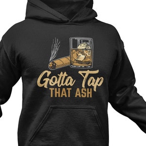Pode incluir: Camisola de moletom com capuz preta com um gráfico de um copo de uísque e um charuto com o texto "Gotta Tap That Ash".