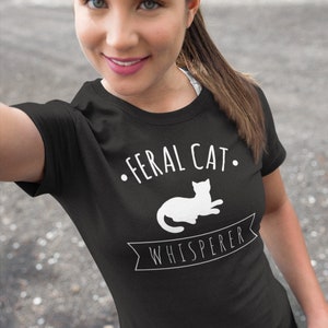 May include: A black t-shirt with white text that reads "Feral Cat Whisperer" and a silhouette of a cat lying down.