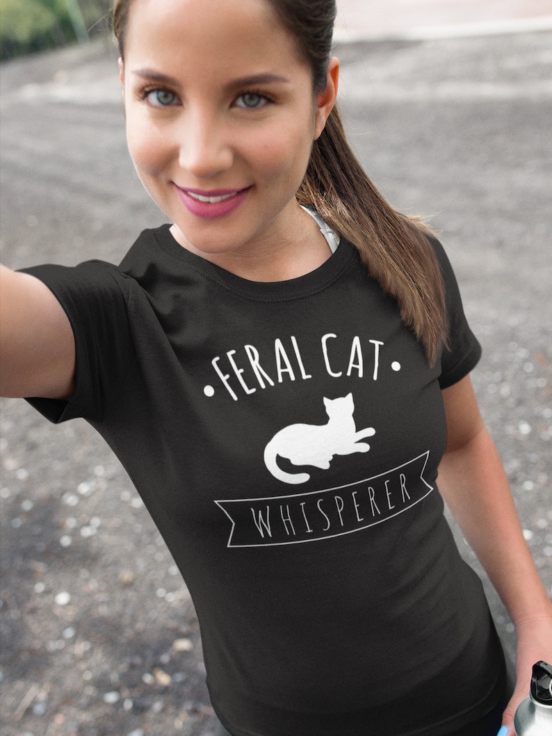 May include: A black t-shirt with white text that reads "Feral Cat Whisperer" and a silhouette of a cat lying down.