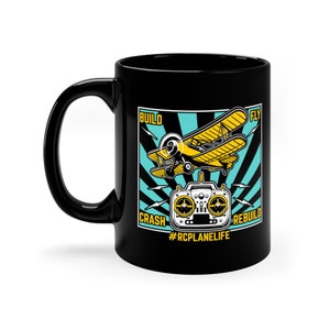 May include: Black ceramic mug featuring a yellow biplane and a remote control graphic. The design includes the words "BUILD, FLY, CRASH, REBUILD" and the hashtag "#RCPLANELIFE". The mug has a curved handle.
