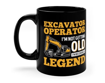 May include: Black coffee mug featuring a yellow excavator graphic and the text "Excavator Operator I'm not getting old I'm becoming a Legend".