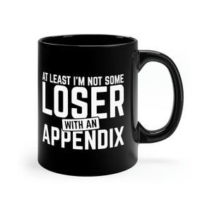May include: Black ceramic coffee mug with white text that reads "At least I'm not some loser with an appendix".