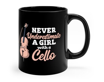 May include: Black ceramic mug featuring the text "NEVER Underestimate A GIRL with a Cello" in white and pink lettering. A cello illustration is on the left side. The mug has a black handle.