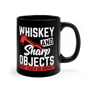May include: Black ceramic mug with the text "WHISKEY AND SHARP OBJECTS" and a red axe graphic. The phrase "WHAT COULD GO WRONG?" is printed below the axe. The mug has a black handle.