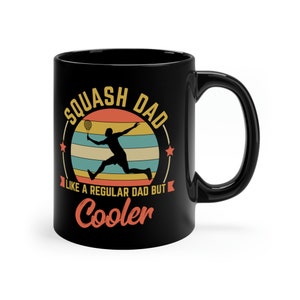 Könnte beinhalten: Schwarze Kaffeetasse mit einer weißen Grafik einer Person, die Squash spielt, mit dem Text "Squash Dad Like a regular dad but Cooler".