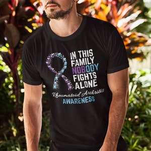 May include: Black t-shirt with a blue and purple ribbon made of hearts. The text on the shirt reads "In this family nobody fights alone. Rheumatoid Arthritis Awareness."