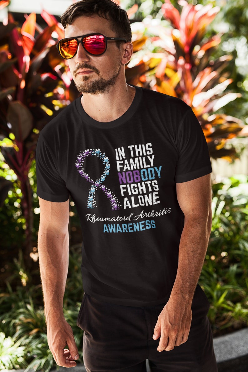 May include: Black t-shirt with a blue and purple ribbon made of hearts. The text on the shirt reads "In this family nobody fights alone. Rheumatoid Arthritis Awareness."