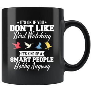 May include: Black ceramic mug with a white handle. The mug features the text "IT'S OK IF YOU DON'T LIKE Bird Watching" and "IT'S KIND OF A SMART PEOPLE Hobby Anyway" in white. Four colorful bird silhouettes are below the text.