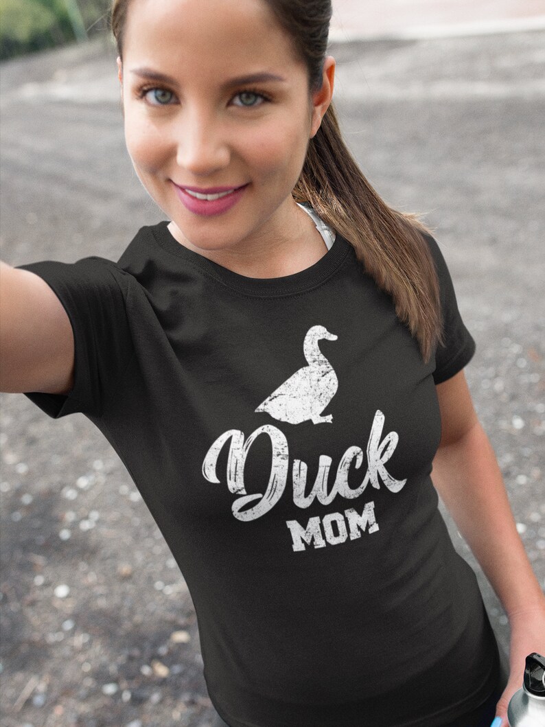 Puede incluir: Una camiseta negra con una silueta de pato blanca y el texto "Duck Mom" en una fuente blanca desgastada.