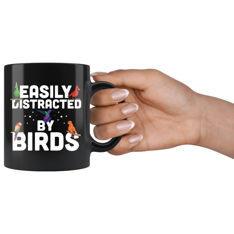 Puede incluir: Taza de cer&aacute;mica negra con el texto blanco "EASILY DISTRACTED BY BIRDS". La taza presenta ilustraciones coloridas de varios p&aacute;jaros. La taza est&aacute; sostenida por una mano con u&ntilde;as cuidadas.
