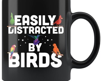 May include: Black ceramic mug with the text "EASILY DISTRACTED BY BIRDS" in white. The mug features colorful illustrations of various birds, including a parrot, cardinal, and hummingbird, perched on branches.