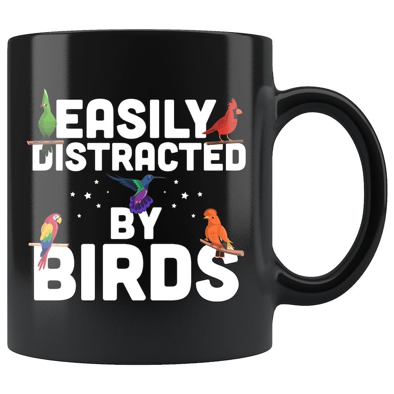 Puede incluir: Taza de cer&aacute;mica negra con el texto "EASILY DISTRACTED BY BIRDS" en blanco. La taza presenta ilustraciones coloridas de varias aves, incluyendo un loro, un cardenal y un colibr&iacute;, posadas en ramas.