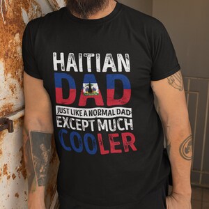 May include: Black t-shirt with the text "Haitian Dad" in white with a distressed effect. The text is layered over a graphic of the Haitian flag. Below the flag is the text "Just like a normal dad except much cooler" in white with a distressed effect.