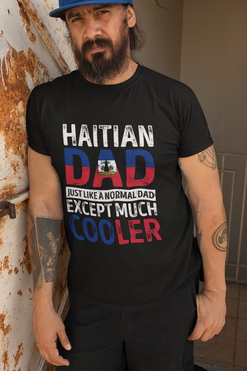 May include: Black t-shirt with the text "Haitian Dad" in white with a distressed effect. The text is layered over a graphic of the Haitian flag. Below the flag is the text "Just like a normal dad except much cooler" in white with a distressed effect.