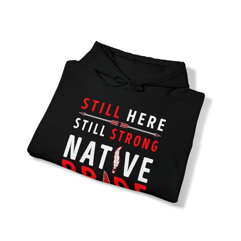 May include: Black hooded sweatshirt with the text "Still Here Still Strong Native Pride" in white with red accents. The text is surrounded by two arrows pointing to the right.
