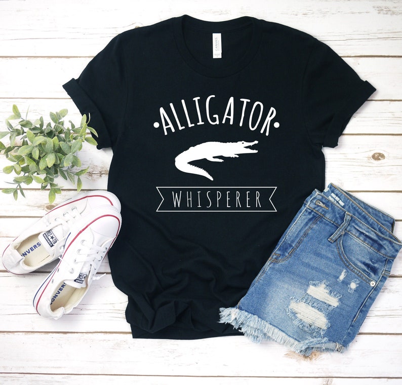 May include: Black t-shirt with a white alligator graphic and the text "Alligator Whisperer".